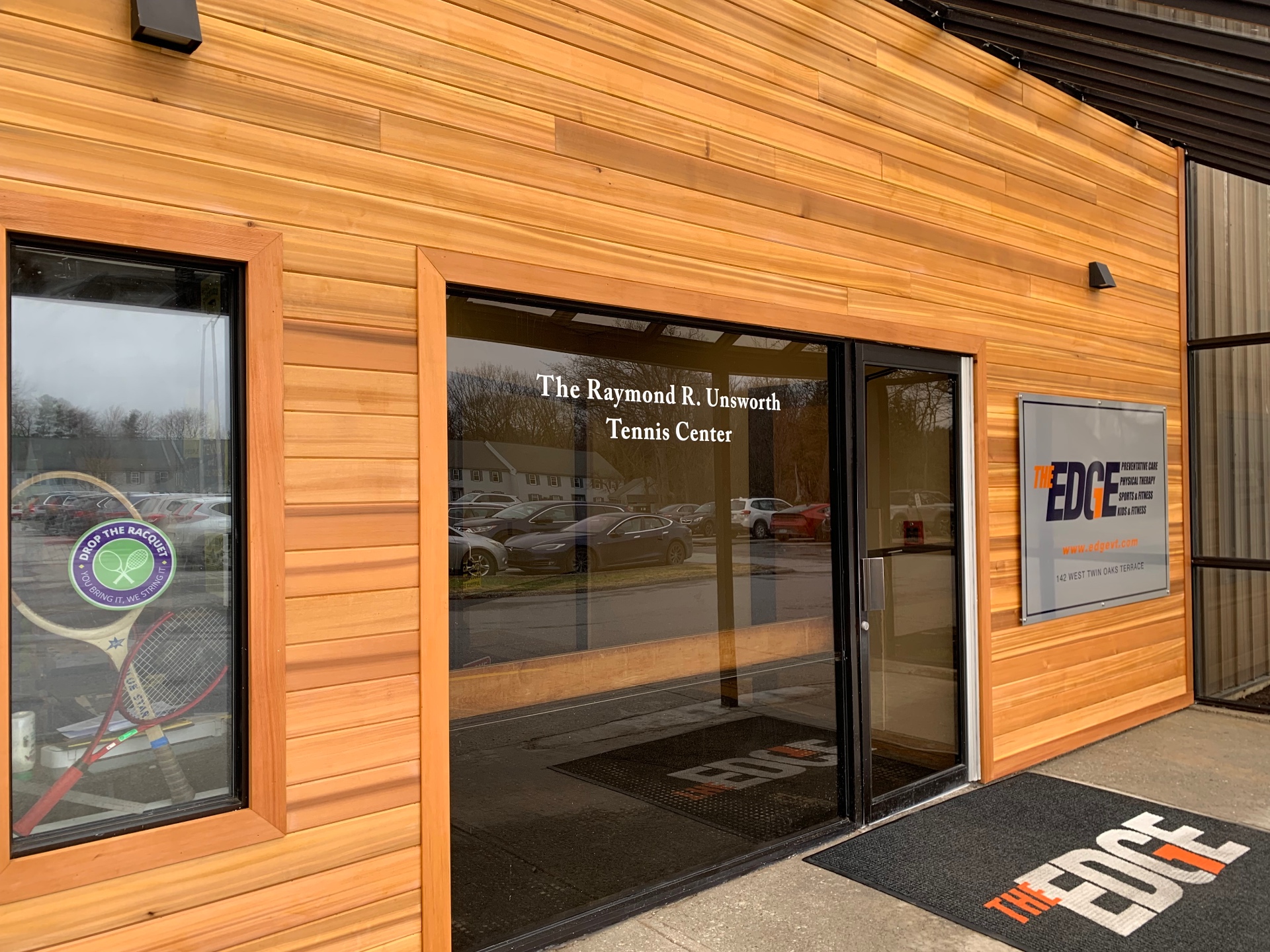 Cedar-clad commercial entrance facade with vertical black steel trim and a lit signage panel at a South Burlington, Vermont fitness facility.